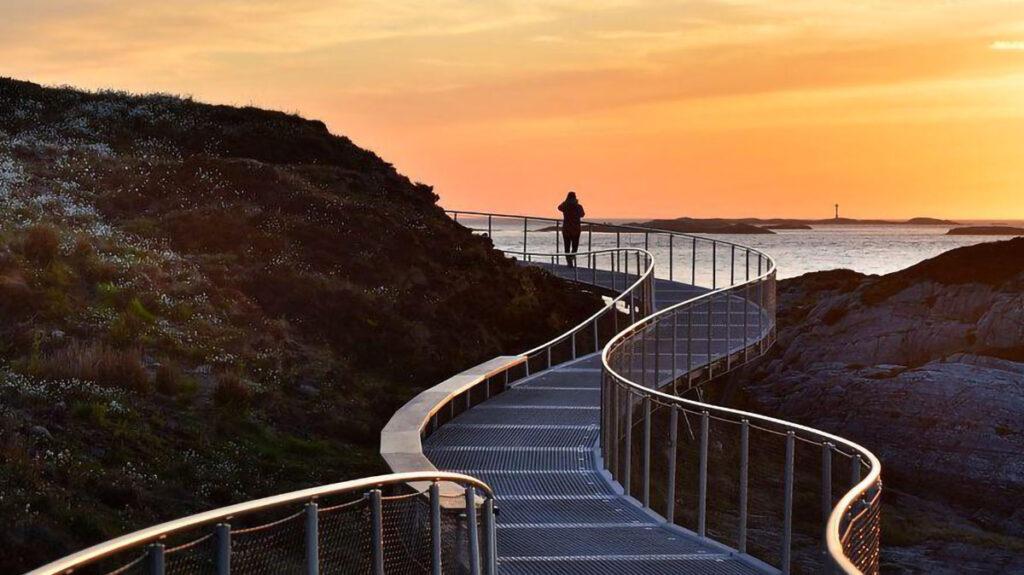 Atlanterhavsveien utsiktsstien på eldhusøya er spektakulær og åpen hele året. bildet viser en mann som går stien i solnedgang