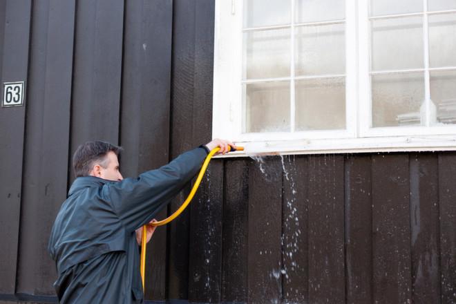 Mann som spyler med slange på husveggen under husvask.