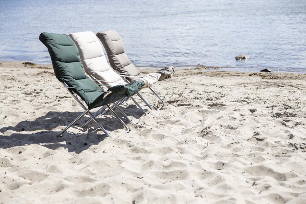 Grønn, hvit og beige solstol på strand ved havet. 