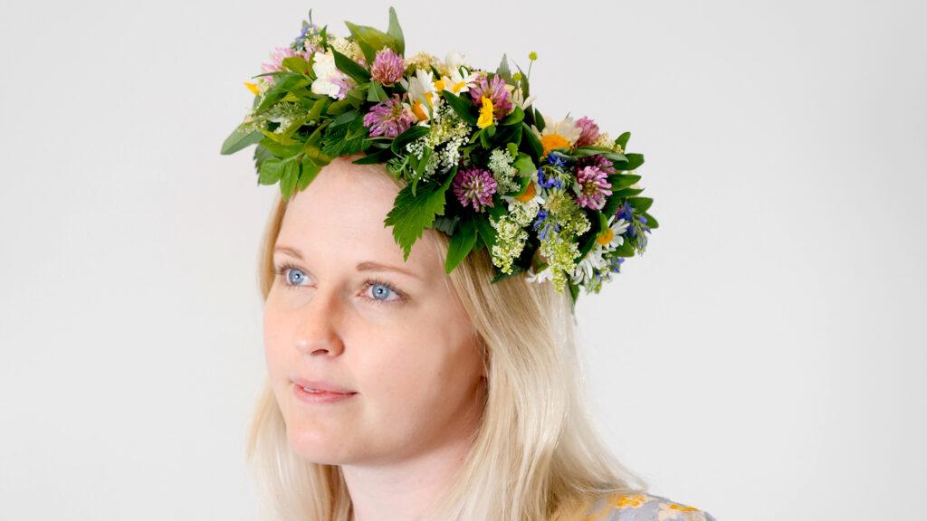 Bilde av kvinne med vakker blomsterkrans i håret, laget av markblomster. Vi viser hvordan du enkelt lager den vakre blomsterkransen selv. Den pynter opp håret til både 17. mai, bryllup, dåp, sankthans og konfirmasjon.  