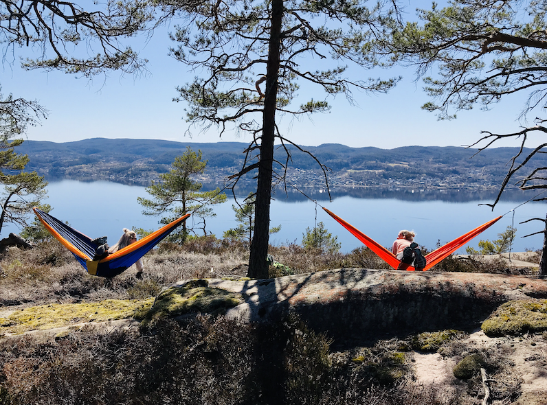 To damer i hver sin hengekøye med utsikt ut over vannet