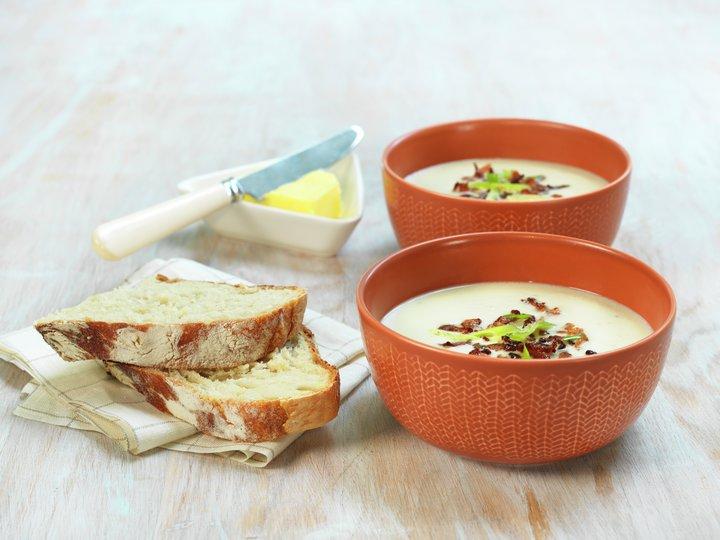 Bilde av blomkålsuppe med brød, sprøstekt bacon og vårløk. Her får du oppskrift på kremet blomkålsuppe med fløte. 