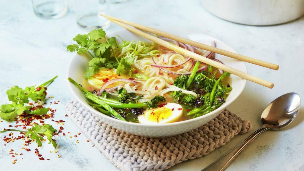 Oppskrift ramen: Bilde av vegetar ramen med egg, nudler, kål, koriander, chili, rødløk, hvitløk og ingefær i skål med spisepinner