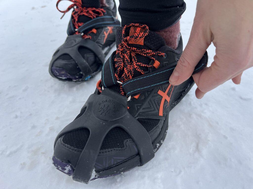 Bilde av peson som strammer stroppene på et par
Nordic Grip-brodder av typen 
Nordic Grip running. Broddene er tredd utenpå et par med svarte joggesko fra Asics med oransje detaljer og lisser og personen står på et snødekket underlag. Vi firteller hvilke brodder som er bst til ulike formål! 