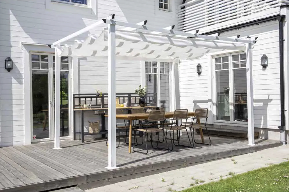 Bilde av en hvit pergola med duk utenfor på terrassen til hvitt hus.