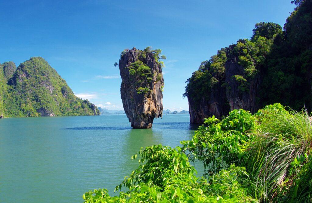 Et ikonisk kalksteinsfjell stiger opp fra det smaragdgrønne vannet i Phang Nga-bukten (også kjent som James Bond Island), omringet av frodige, grønne øyer og vegetasjon, med en klar blå himmel i bakgrunnen. Vi hjelper deg med å finne reise til Thailand, enten du vil ha billige reiser med restplasser, eller kanskje pakkereiser til de populære destinasjonene Phuket, Hua Hin og Krabi. Her finner du også hotell i Thailand.