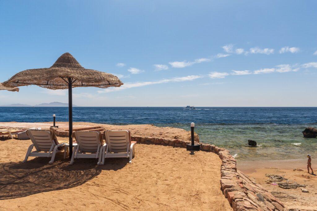 Solsenger under en parasoll på en strand i syden, i bakgrunden ser man blått hav. Vi har samlet restplass all inclusive-reiser til populære destinasjoner som Hellas, Gran Canaria, Tyrkia, Mallorca, Tenerife og Kroatia.