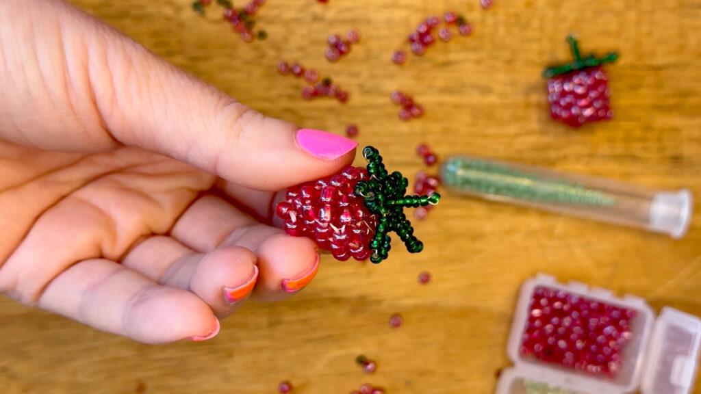 Et jordbær eller bringebær laget av røde og grønne perler.