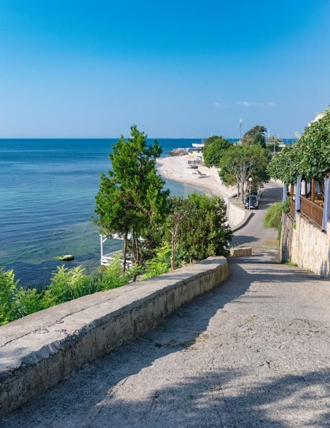 Bilde av en gate i Nessebar hvor du ser havet på venstre side og noen hus på høyre side, og en strand i bakgrunnen. Her finner du billige reiser til Bulgaria til populære destinasjoner langs kysten som Nessebar og Sunny Beach.