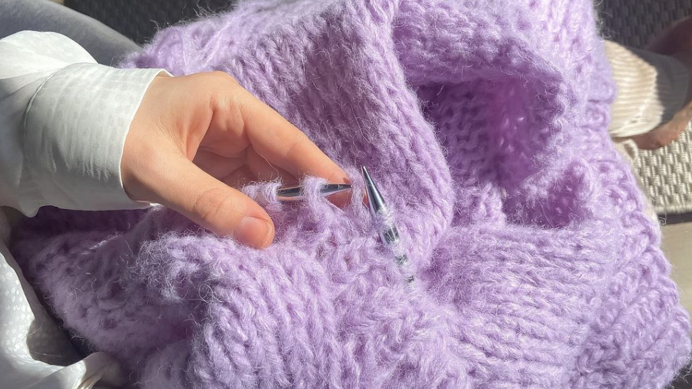 Lilla strikket genser i fluffy garn. Dame som holder strikketøy. Strikkeoppskrift for nybegynnere.