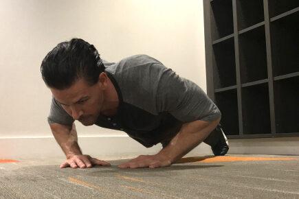 Bilde av personlig trener Cornelis Elander som trener armhevinger/ diamond push-ups på treningsmatte. Han har på seg en grå t-skjorte, en blå treningsbukse og befinner seg i et treningsrom. Dette er en styrkeøvelse med fordeler for hele kroppen, og er en av styrkeøvelsene i vårt 30-dagers gratis treningsprogram og styrkeprogram.