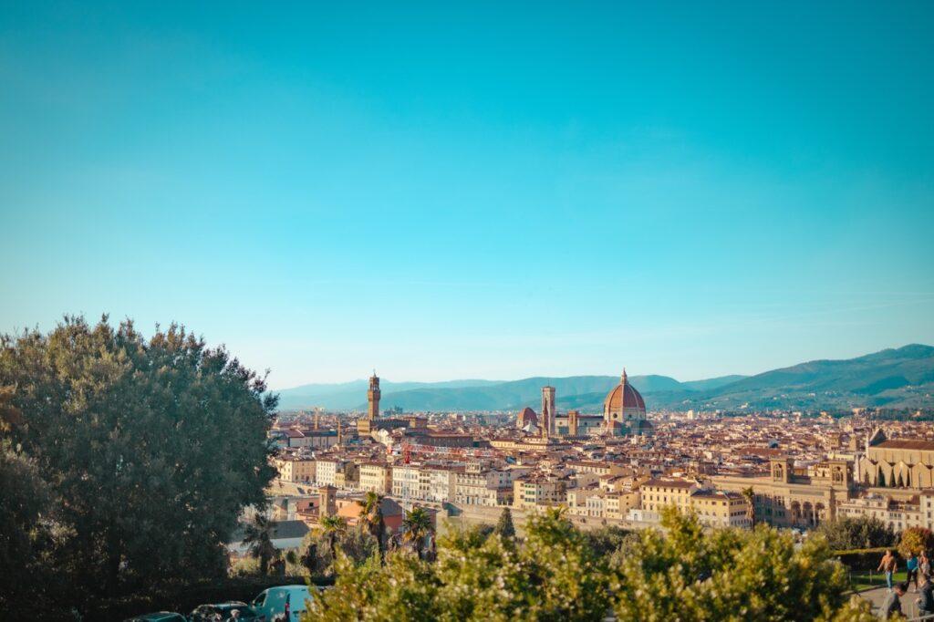 Utsikt over Firenze, Italia, på en solrik dag med en klar blå himmel. I sentrum av bildet dominerer den ikoniske katedralen Santa Maria del Fiore med sin store kuppel, omgitt av historiske bygninger og kirker. Bakgrunnen viser de bølgende åsene i Toscana. Vi har laget en omfattende guide til Toscana i Italia hvor vi blant annet forteller om fem populære byer som Firenze, Pisa, Siena, Montepulciano og Volterra. Vi gir deg også forslag til tre kjøreruter du kan ta for å oppleve vingårder og resten av Toscana. La deg inspirere av den italienske regionen som fikk sitt eget TV-program; «Den store matfesten - Toscana»