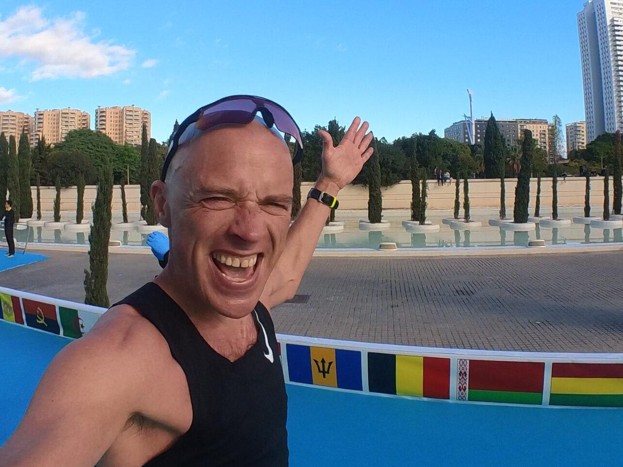 Bildet viser en entusiastisk løper som nærmer seg målstreken under Valencia Maraton. Løperen er iført en svart singlet, solbriller på hodet, og en grønn løpslapp med navnet "Andy" festet til shortsen. Han har armene løftet i triumf og smiler bredt, tydeligvis fornøyd med prestasjonen. Bakgrunnen viser en klar blå himmel, høye bygninger og trær, samt en blå løper som dekker løpsbanen. Det er også internasjonale flagg langs banen som gir en følelse av global deltakelse. Bildet fanger et øyeblikk av glede og seiersfølelse etter en imponerende fysisk innsats. Løpetrener Andreas Gossner fra løpetrening.no forteller Hvilke muligheter har du som er passert 60 år og er glad i løping har? Løpetrener forteller hvordan du kan opprettholde løpetreningen!