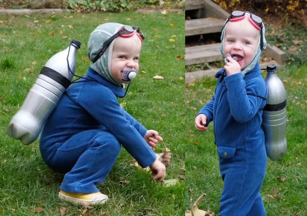 Bildet viser et lite barn kledd ut som dykker med et kreativt, hjemmelaget kostyme. Barnet har på seg en blå heldress og en grå lue med påsydde dykkebriller. På ryggen er to sølvmalte plastflasker festet som oksygentank, holdt på plass med svart snor. Smokken i munnen fungerer som en morsom detalj i kostymet. Barnet leker ute i gresset og smiler, tydelig fornøyd med sin fantasifulle utkledning.