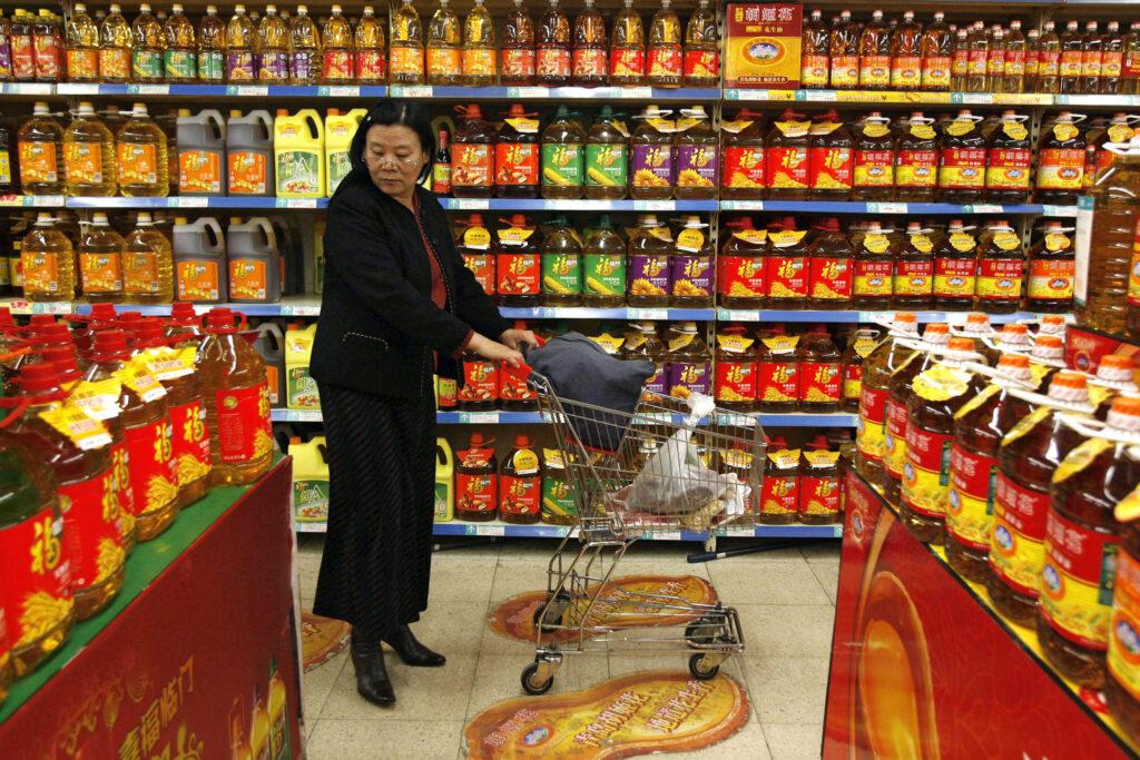 En kinesisk kunde undersøker priser på matolje i en supermarkedshylle fylt med forskjellige matoljemerker i Shenyang, Kina.