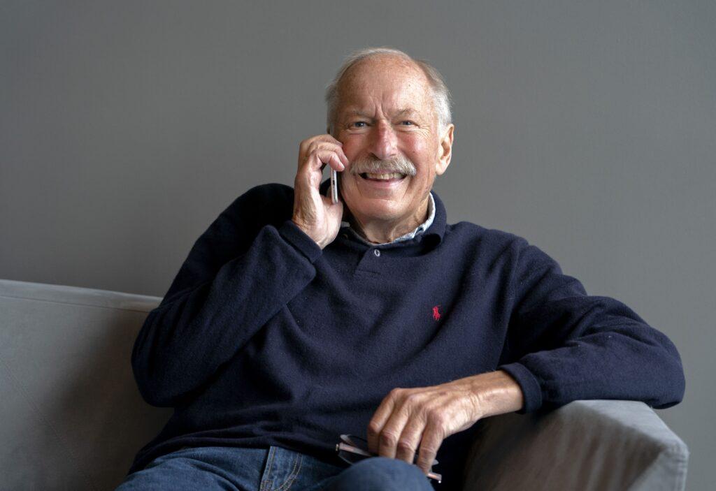 Johan Kaggestad smiler og holder en mobiltelefon til øret mens han sitter avslappet på en sofa.