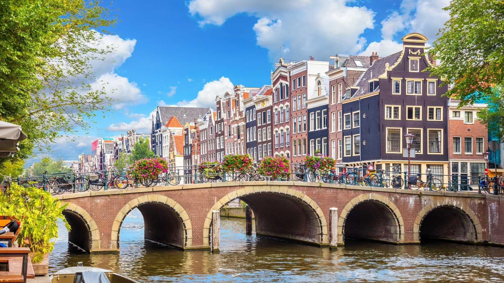 bilde av amsterdams mange kanaler. på bilde ser du en kanal, en bru og klassiske amsterdam hus.