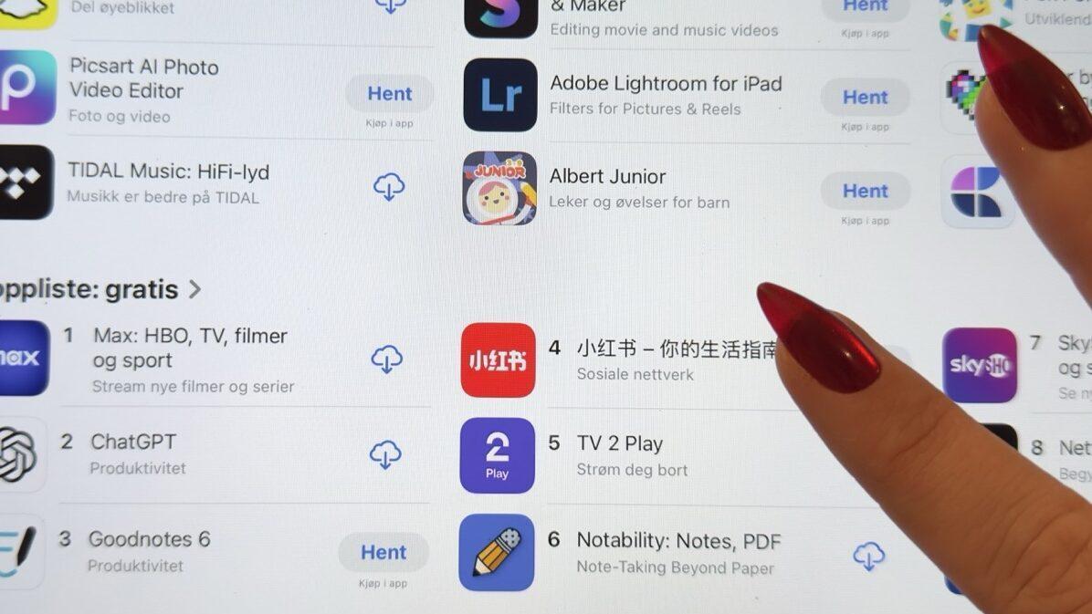 Skjermbilde fra en app-butikk som viser seksjoner med populære apper. Under kategorien «Apper vi elsker for tiden» er apper som Snapchat, Picsart AI Photo Video Editor og TIDAL Music oppført. I seksjonen «Toppliste: gratis» vises de mest nedlastede gratisappene, hvor Max (HBO, TV, filmer og sport) er rangert som nummer én, fulgt av ChatGPT på andreplass og Goodnotes 6 på tredjeplass. Videre nedover ligger appene 小红书, TV 2 Play og Notability. En hånd med lange røde negler peker mot skjermen.
