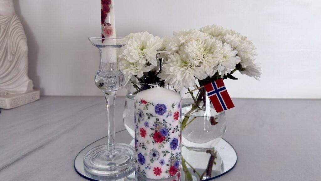 Dekorerte lys med 17. mai-servietter og hvite blomster skaper en elegant og personlig borddekorasjon. Lag dine egne lys med serviett og strykejern – en enkel og miljøvennlig DIY-idé for festbordet.