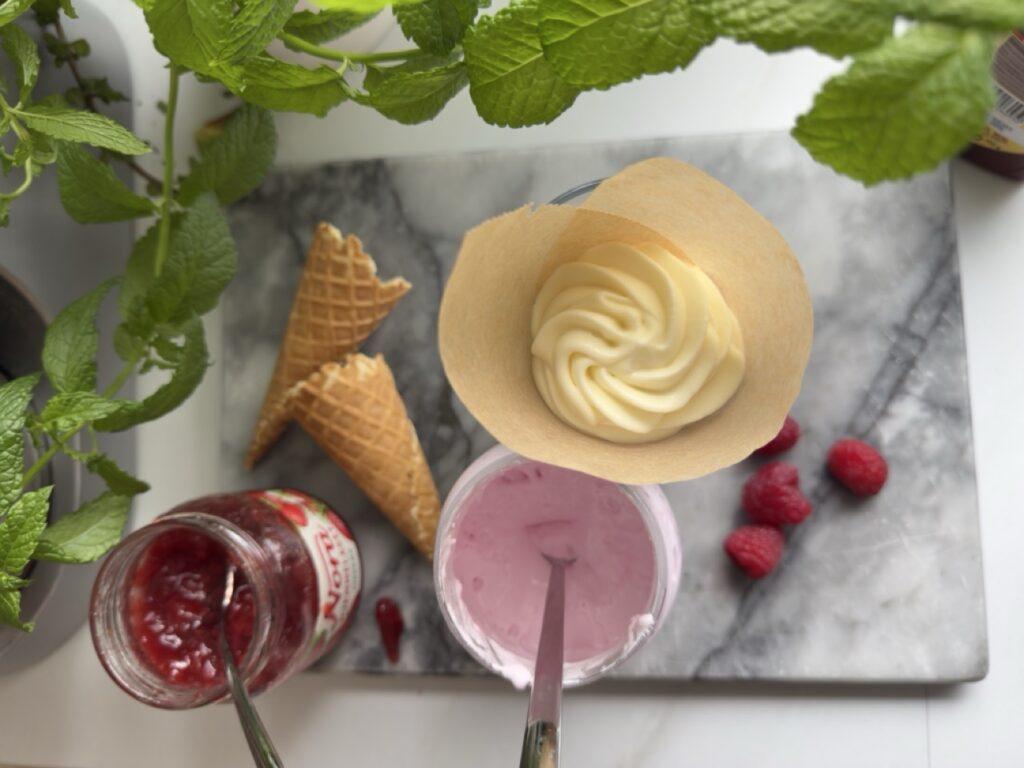Isen fylles lagvis med marshmallow Fluff og bringebærsyltetøy for en dansk-inspirert “guf”-kroneis. Friske bringebær og vaffelkjeks venter på å bli til en fargerik sommerfavoritt.