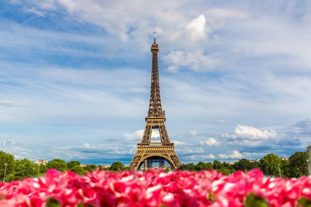 Bilde av Eiffeltårnet i Paris. I forgrunnen ser du rosa blomster og i bakgrunnen er det en blå himmel. Vi gir deg en omfattende guide til kjærlighetens by som kan by på alt fra Triumfbuen, Louvre, Notre-Dame, Disneyland Paris og mye mer.