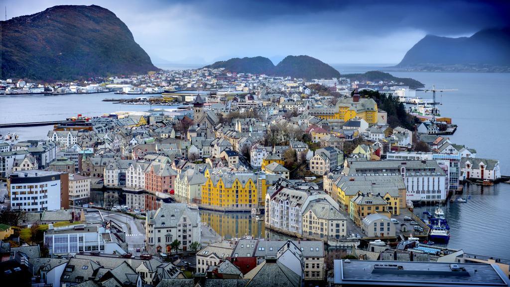 Helbilde av Ålesund i skumring med fjell og fjord i bakgrunn.