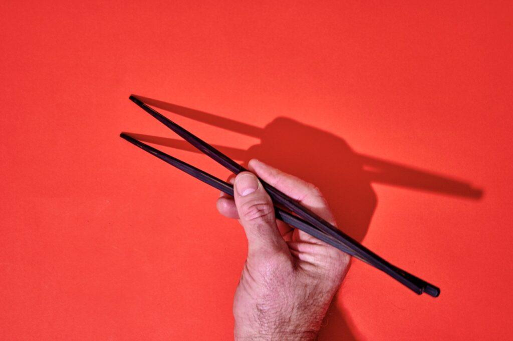 Med dette smarte trikset lærer du deg å holde spisepinner på 1-2-3. Hånd som holder spisepinner foran rød bakgrunn.