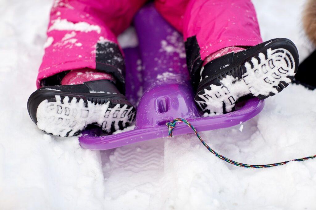Bilde av barn på akebrett, ute i snø, med sorte og rosa vintersko(cherrox) og rosa vinterbukse. Vi forteller hvilke støvler og vintersko som er best i test til barn i 2023, fra merker som Kavat, Sorel, Crocs, Bisgaard og Helly Hansen.