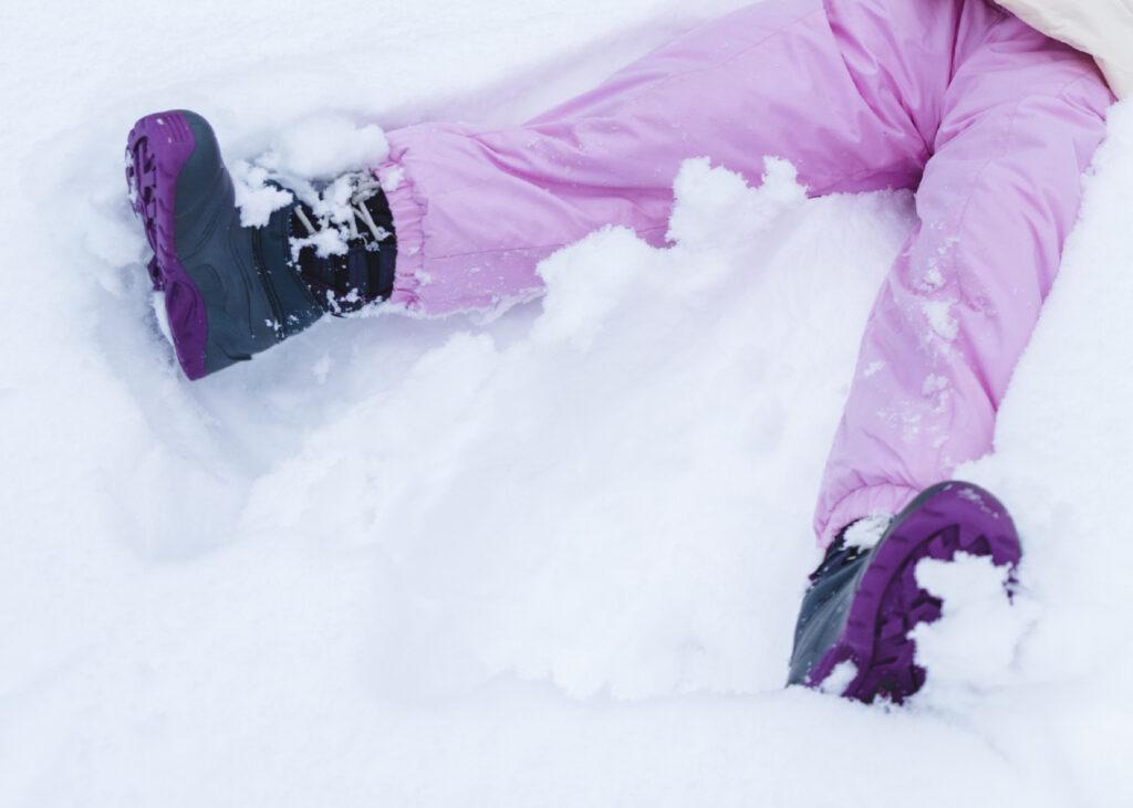 Bilde av barn med sorte og lilla vintersko og rosa vinterbukse som leger in snøen.