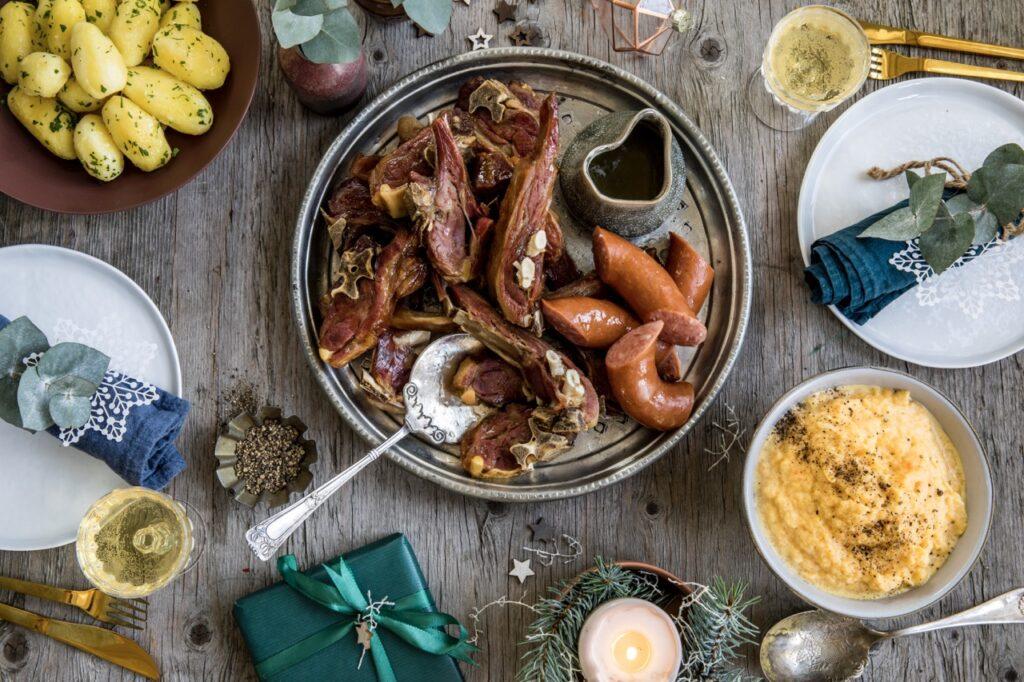 Et bord dekket til julemiddag med pinnekjøtt, rotmos, vossakorv og poteter.