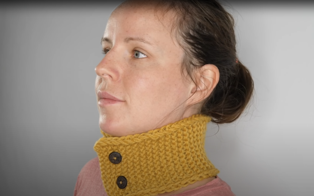 Bilde av dame med flott gul, selvstrikket hals med treknapper. Her får du strikkeoppskrift på strikkehalsen til dame og barn.