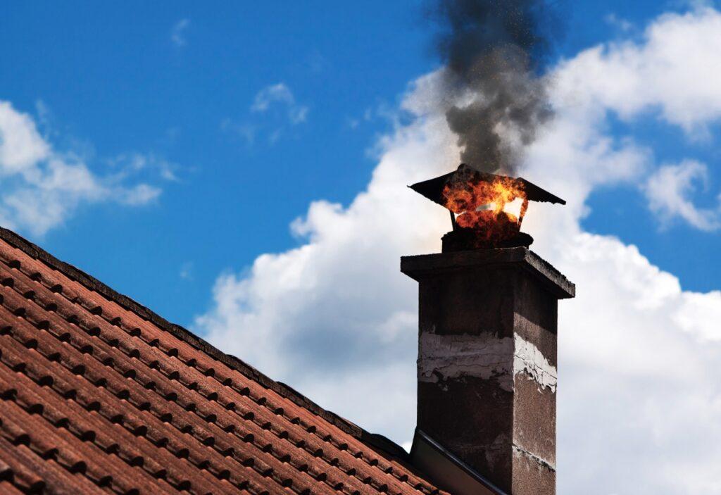 Bilde av pipe med brann på rødt tak og med blå himmel i bakgrunn.
