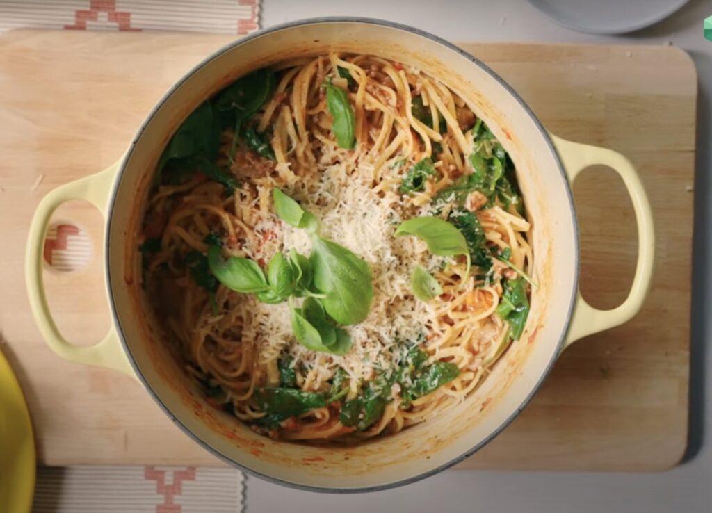 Bilde av one pot pasta i beige jerngryte på fjøl, med parmesanost og frisk basilikum