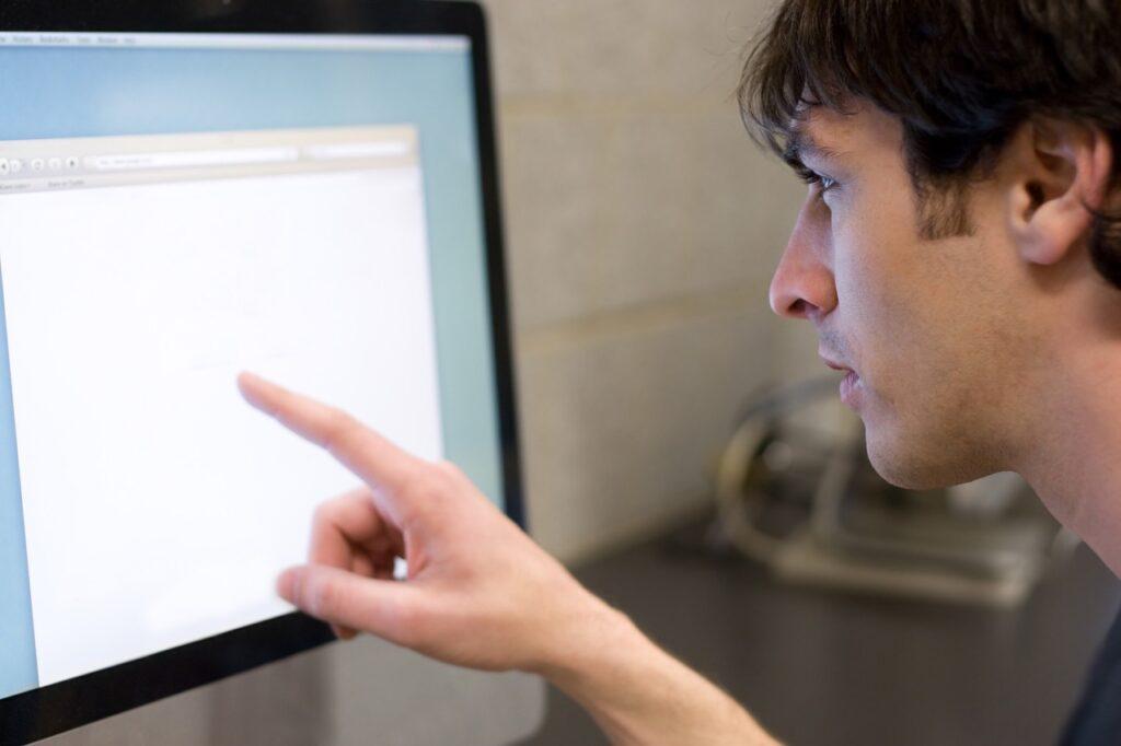 Bilde av mann som tar fingeren opp for å se nøyere på noe på en dataskjerm. Vi forteller at nå er det vedtatt at man snart kan sjekke skattelister anonymt.