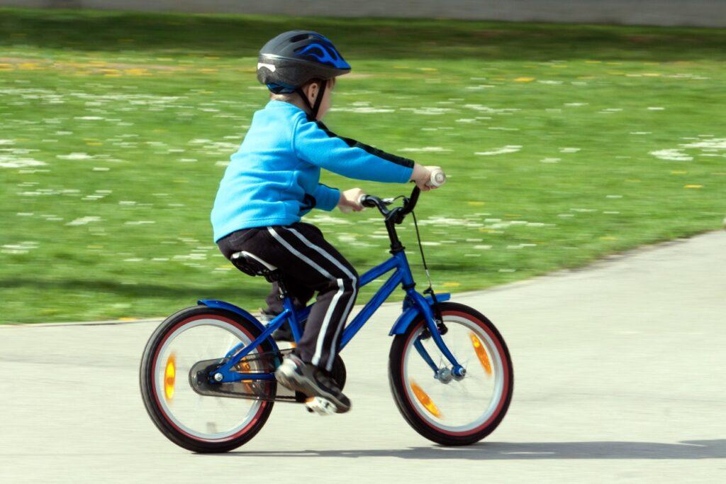 Et barn med blå genser og sykkelhjelm sykler på en blå sykkel. Vi forteller det du trenger å vite om elsykkel til barn.