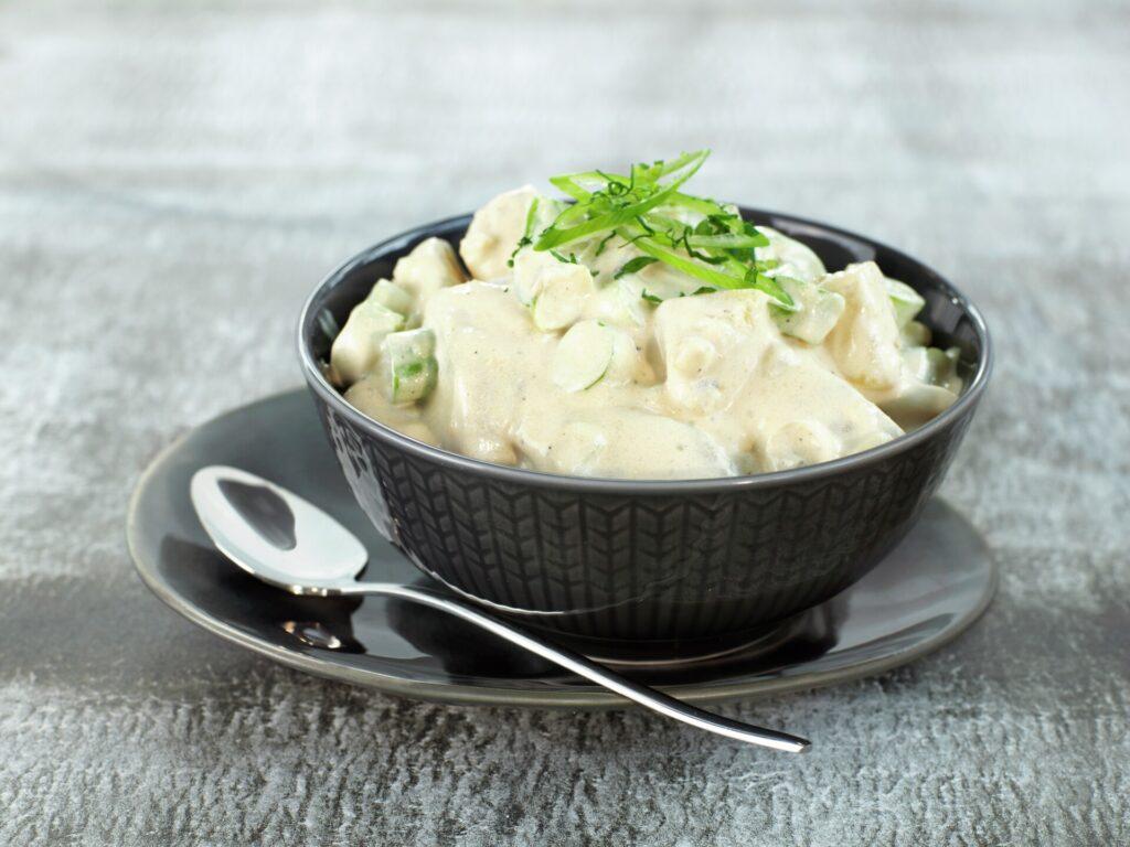 Potetsalat: En skål med klassisk potetsalat på et bord. Vi gir deg oppskriften på tilbehøret som passer til både 17. mai, konfirmasjon, bryllup, dåp, koldtbord, grillmiddager og sommerfester.