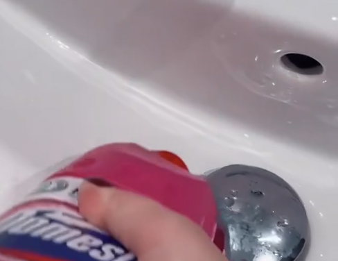 Bilde av tett sluk i vask med en hand som sprøyter domestos wc-rengjøring i sluket for å åpne det.