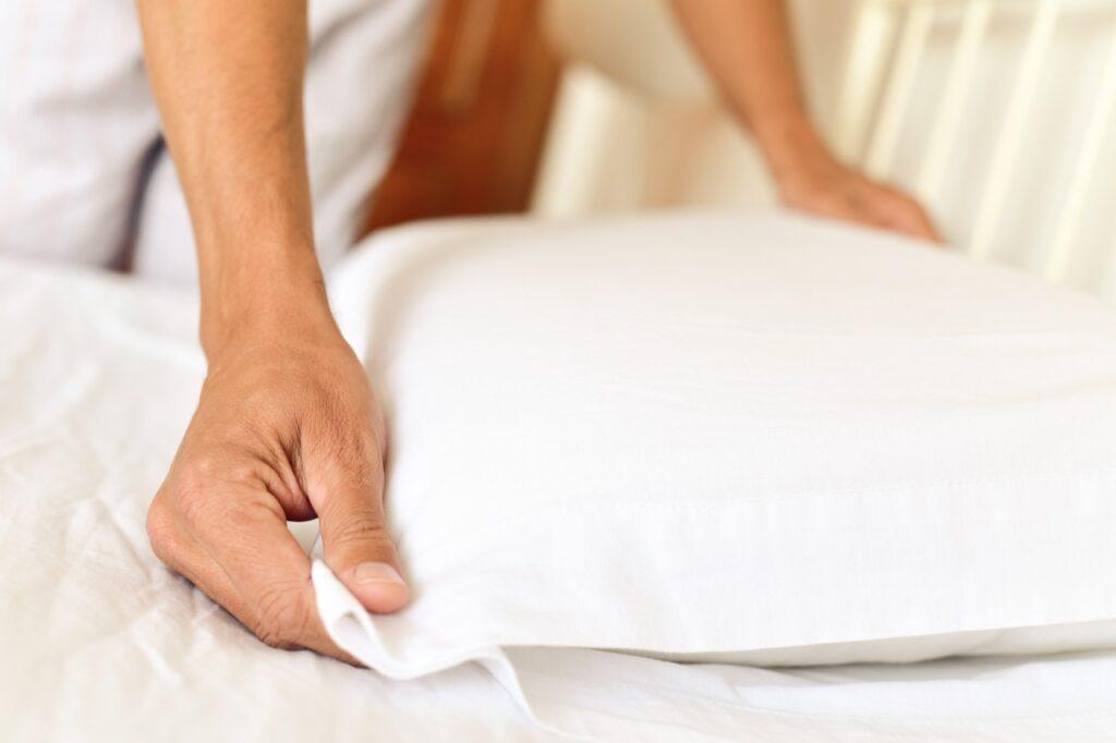 Skifte sengetøy: En person holder i en hvit pute mens hen rer opp en seng.