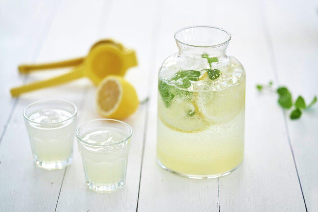 Limonade med sitron: En karaffel og to glass med limonade på et hvitmalt bord. her får du oppskrift på det som kanskje er verdens beste og mest smakfulle limonade.