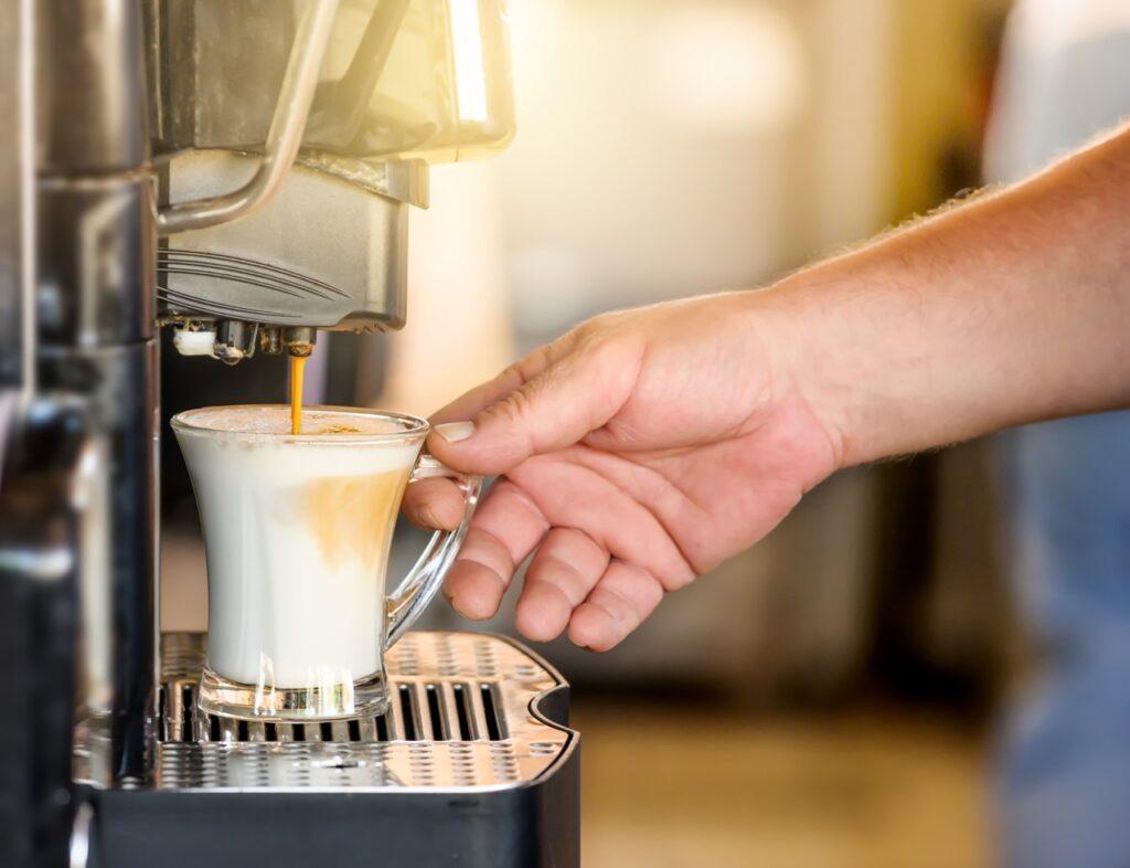 Nærbilde av en kaffemaskin som serverer kaffe med melk i en glasskopp. Vi har sett på espressomaskiner, kapselmaskiner og kaffetraktere for å finne kaffemaskinen som er best. Populære merker som Smeg, Wilfa, Moccamaster, Siemens, Nespresso og De'longhi er blant de mange testvinnerne.