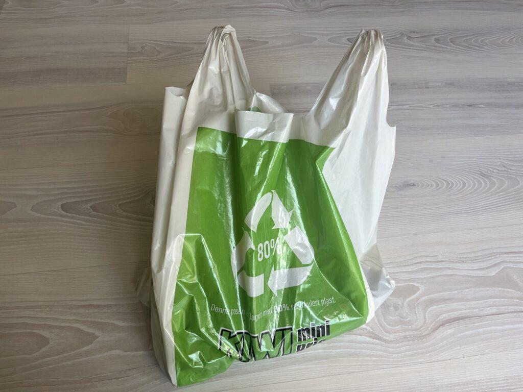 Bilde av grønn og hvit plastpose fra Kiwi på stuegulv. Vi skriver om nyheten om at prisen på plastposer nå øker.