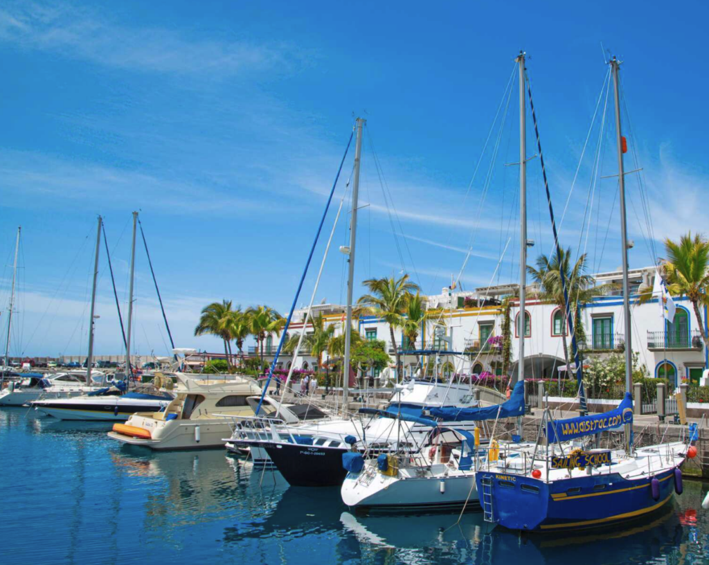 Bilde av båter i havn på Gran Canaria, med sol og blå himmel. Vi forteller hvordan du kan sikre deg billige restplasser til Gran Canaria. Nå kan du sikre deg en billig reise med restplass til gran canaria. Restplasser til Gran Canaria kan være en fin måte å finne en billig reise til varmere strøk. Vi har samlet billige restplasser i 2023 på både hotell og fly.