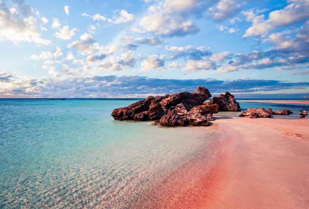 Bilde av Elafonissi-stranden på Kreta i Hellas som er kjent for sin rosa sand i kontrast med krystallklart hav. Vi har funnet restplasser til Kreta slik at du kan nyte billig reise til Hellas. Vi gir deg også fem tips til ting du må se og gjøre på den vakre øya, blant annet: Knossos, Samariaravinen, Elafonissi, Rethymnon og Spinalonga.