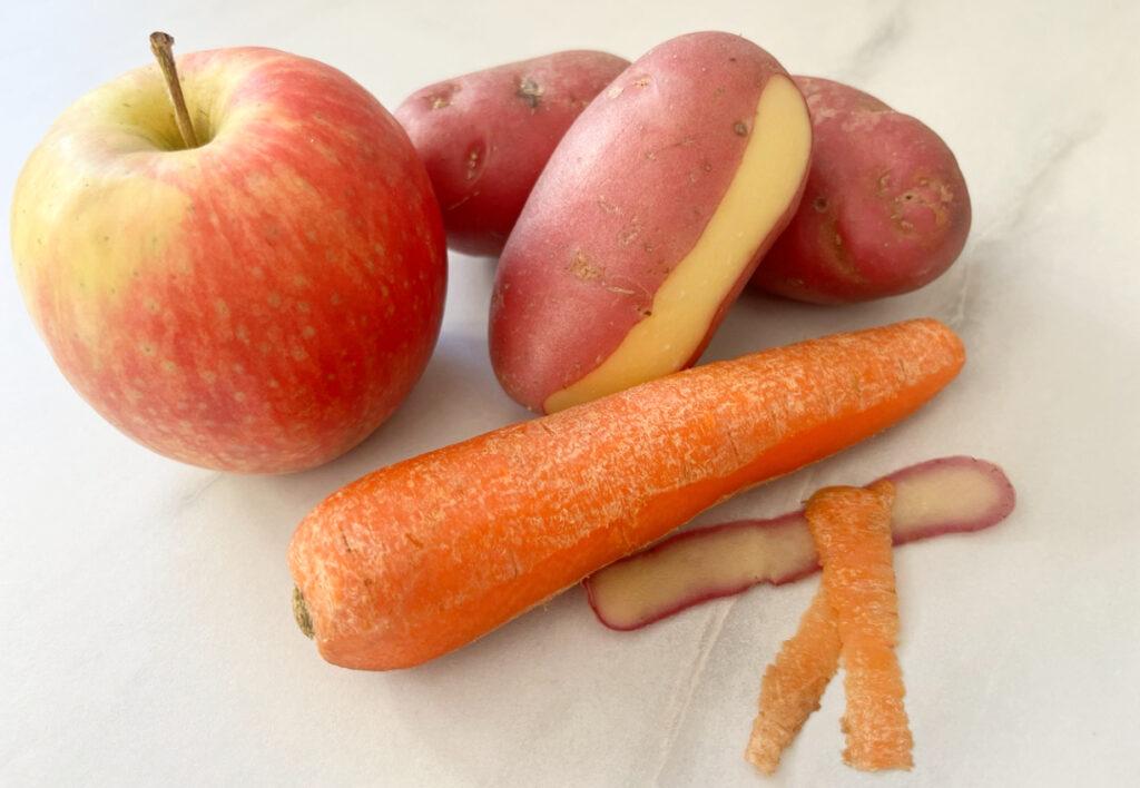 Bilde av frukt og grønnsaker, nærmere bestemt et eple, en gulrot og tre poteter, til saken «Derfor må du ikke skrelle frukten og grønnsakene dine». Ja, for du skreller vel ikke grønnsakene dine før bruk? Næringen sitter nemlig i og nær skallet! Vi forklarer hvilke det gjelder!