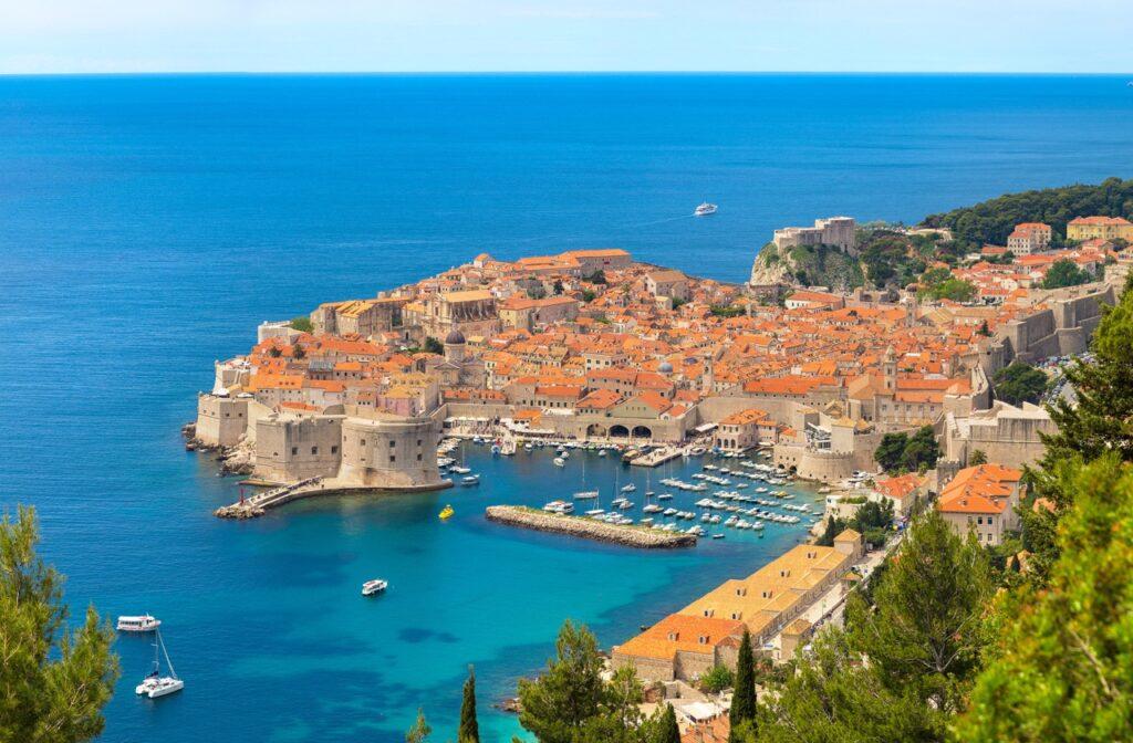 Utsiktsbilde av Dubrovnik i Kroatia. Her ser du den historiske byen som består av historiske severdigheter og murhus med rødt tak, og som er omringet av blått hav. Dubrovnik byr på alt fra vakre strender til historiske severdigheter som Fort Lovrijenac, som også har blitt brukt som sett i den populære serien Game of Thrones.