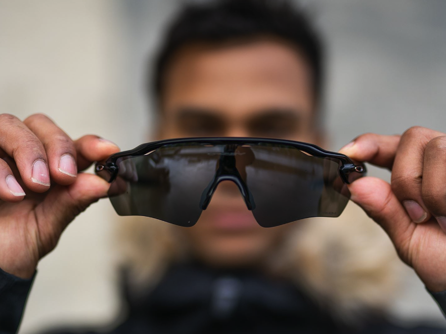 Bilde av en person som holde opp et par solbriller til trening fra Oakley. Vo har snakket med en løpeekspert fra løpetrening.no som forteller hvordan du velger riktige solbriller til treningen din, enten solbrillene er til dame, herre eller barn!