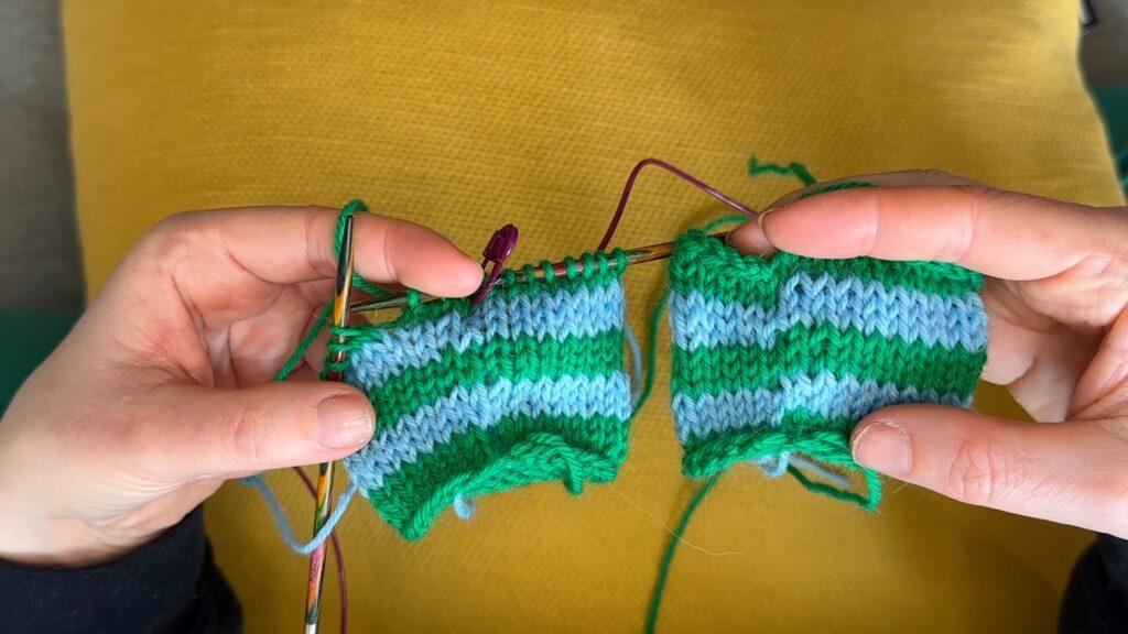 Hender som holder to nesten like små strikketøy med striper i grønt og blått. Strikketøyet til venstre har nesten usynlige overganger i fargeskiftene, mens strikketøyet til høyre ikke har det.