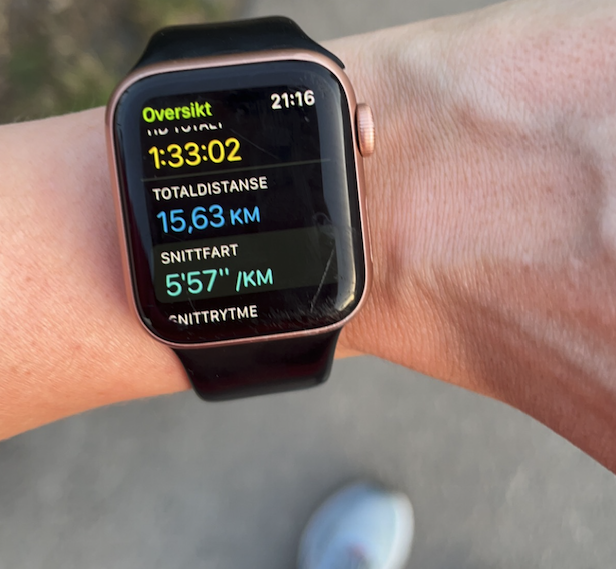 Bilde av en hand med en apple-smartklokke som viser distanse, tid og lengde på en 15 kilometer. Damen har på seg blå løpesko fra Hoka og en grå treningstights. Løpeekspert Andreas Gossner forteller hvor fort man kan løpe 10 km på, både som nybegynner og erfaren. Han forteller også hvordan du kan løpe raskere på 10 km.