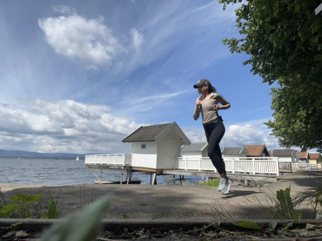 En kvinne som jogger ved sjøen. Hun har på seg en beige treningstop, svarte tights, og en svart caps. Hun har også en smartklokke på håndleddet. Bakgrunnen viser flere badehus på Nesoddens kysststi, Oslofjorden og trær. Solen skinner, og det er en lys og fin dag. Løpeekspert Andreas Gossner fra Løpetrening.no gir deg svaret på om du egentlig må løpe intervaller for å bli god løper, samt hvor ofte du bær løpe intervaller etter hvor mange løpeøkter du har i uken.