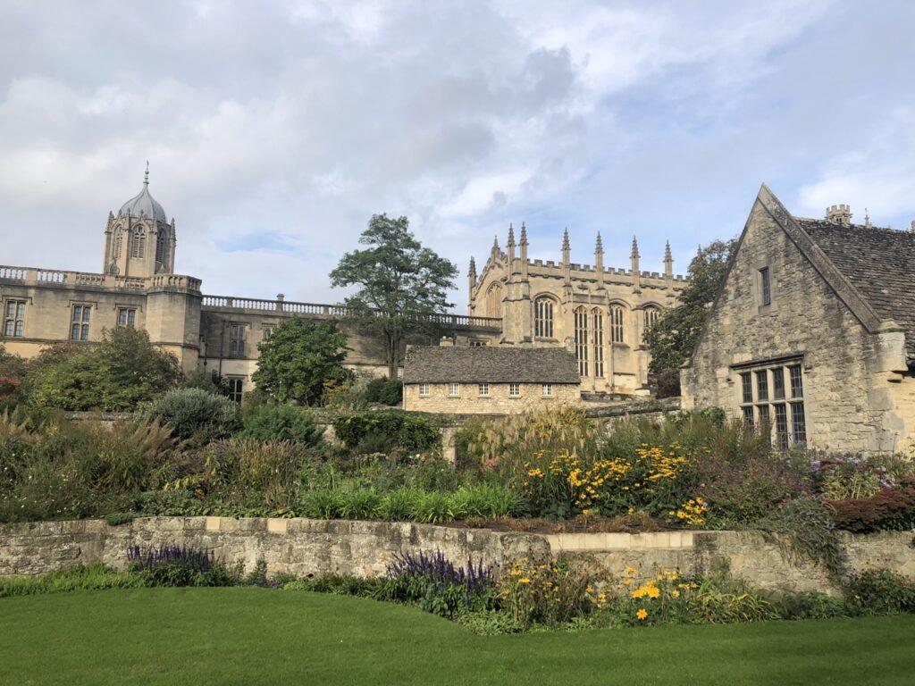 En hage i Oxford, England, med vakre blomster og grønne plener. Bakgrunnen viser gamle, historiske bygninger og Christ Church, alt under en lett overskyet himmel. Vi har samlet fem flotte dagsturer fra storbyen London i England, her finner du inspirasjon til turer til blant annet Oxford, Bath, Brighton, Stonehenge og Windsor Castle.